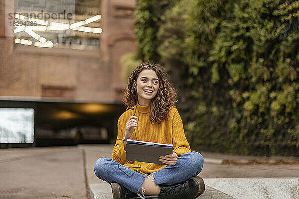 Glückliche Frau mit Tablet-PC sitzt vor dem Gebäude