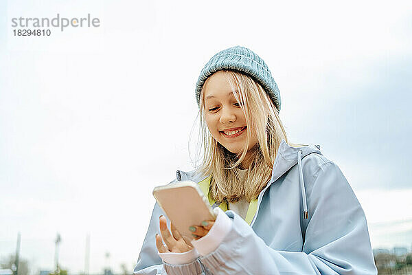 Fröhliches Teenager-Mädchen mit Strickmütze und Mobiltelefon