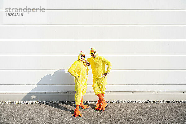 Freunde in gelben Hühnerkostümen stehen zusammen vor einer weißen Wand