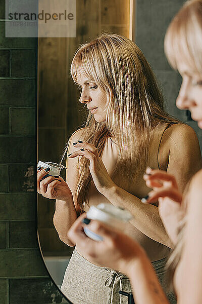 Blonde Frau hält Feuchtigkeitscremebehälter im Badezimmer