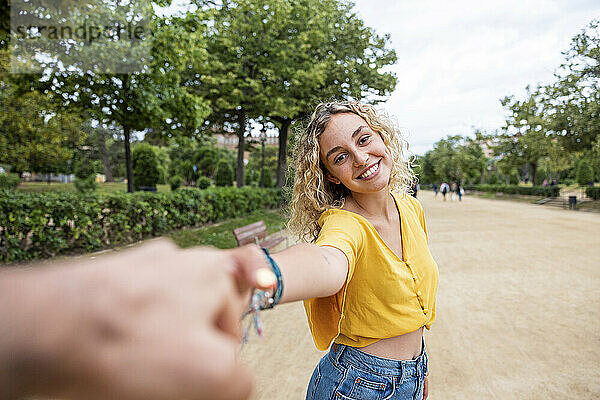 Smiling woman holding friend's hand in park