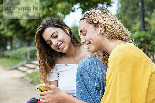 Lächelnde Frau  die im Park ihr Mobiltelefon mit einer Freundin teilt