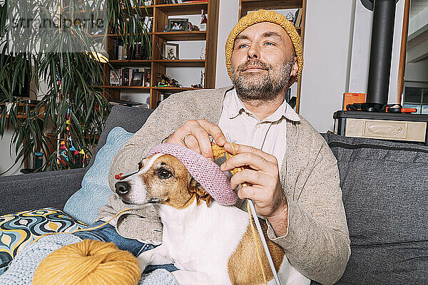 Mann mit Hund strickt zu Hause auf der Couch