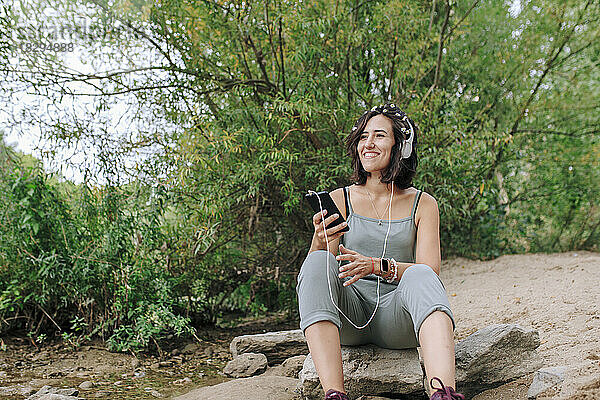 Glückliche junge Frau mit Kopfhörern  die im Park Musik hört