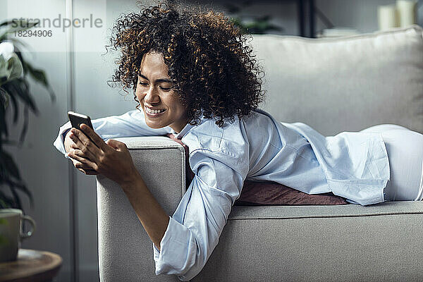 Glückliche Frau  die Textnachrichten über ihr Smartphone sendet und auf dem Sofa liegt