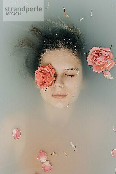 Girl with eyes closed taking bath with roses in bathtub