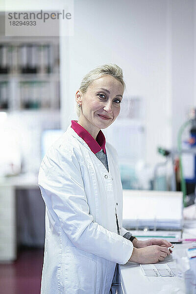 Lächelnder Wissenschaftler steht am Schreibtisch im Labor
