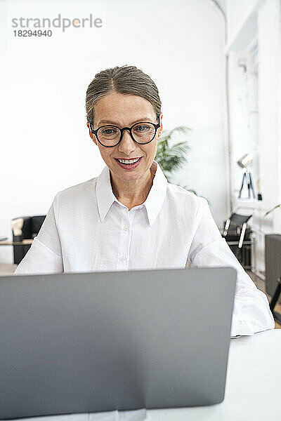 Glückliche Geschäftsfrau mit Brille und Laptop im Büro