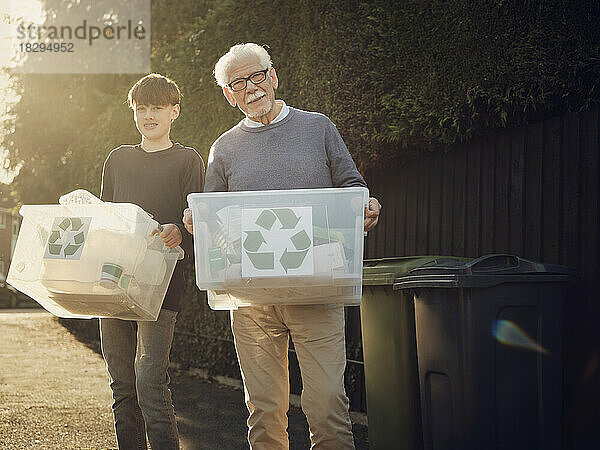 Grandfather and son standing outdoors carrying recycling boxes with separated waste