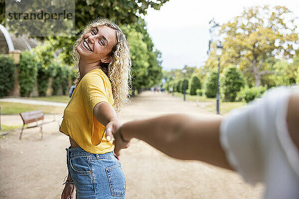 Glückliche junge Frau hält Freunde an der Hand im Park