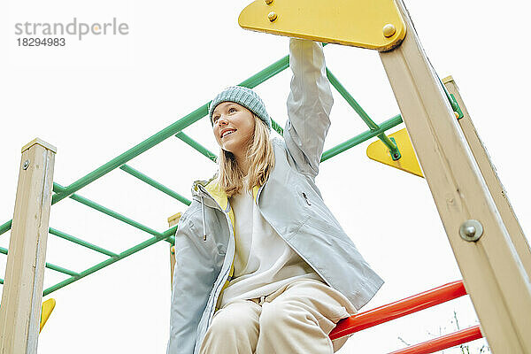 Glückliches Teenager-Mädchen sitzt auf dem Klettergerüst auf dem Spielplatz