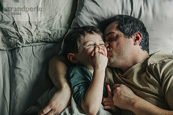 Father kissing cute son in bed