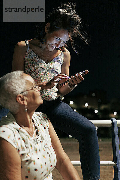 Glückliche junge Frau benutzt Smartphone mit Freund  der im Park sitzt