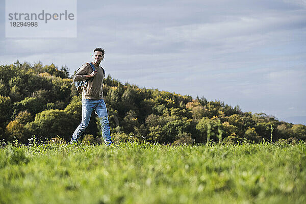 Reifer Mann mit Rucksack wandert auf Gras unter Himmel