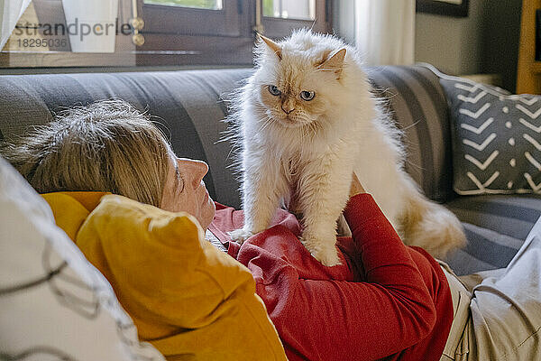 Frau mit Katze liegt zu Hause auf dem Sofa