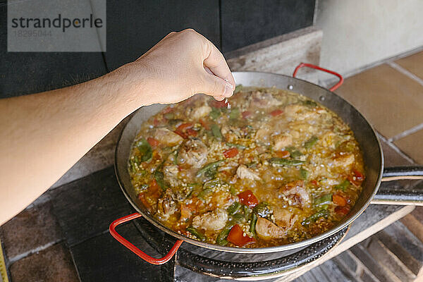 Hand of man adding preparing paella at outdoor kitchen