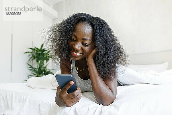 Glückliche Frau  die zu Hause im Bett liegt und ihr Mobiltelefon benutzt