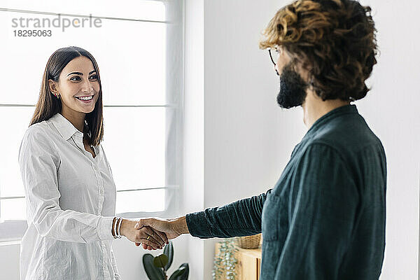 Glückliche Geschäftsfrau schüttelt einem Geschäftsmann im Büro die Hand