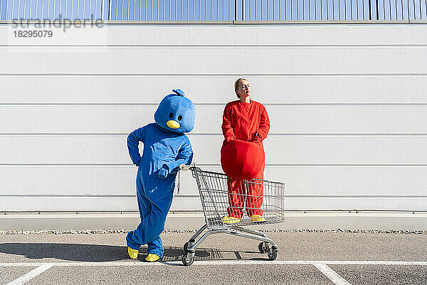 Frau im Kostüm steht an sonnigem Tag mit Mann im Einkaufswagen