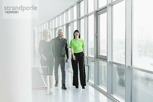Three happy business people in green clothing walking on office floor