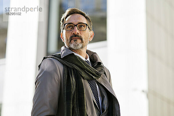 Contemplative businessman wearing eyeglasses in front of office building