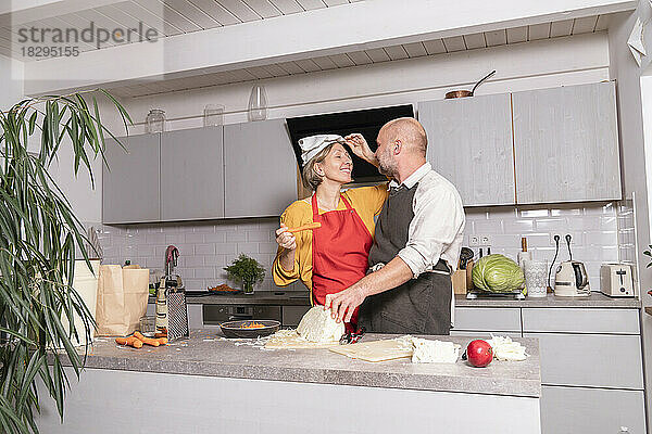 Paar trägt Schürzen und bereitet zu Hause in der Küche eine gesunde Mahlzeit zu