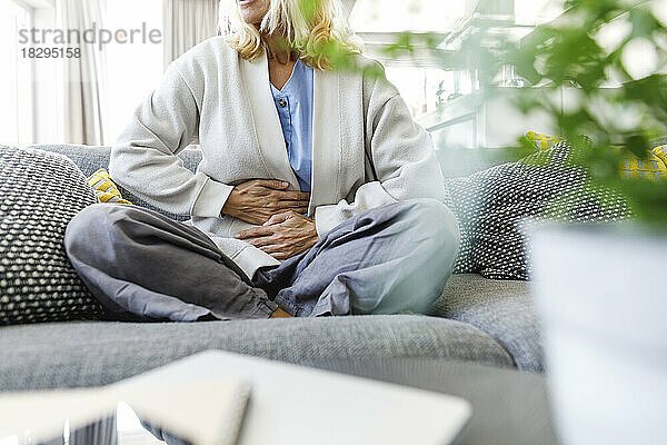 Frau mit Bauchschmerzen  die zu Hause auf dem Sofa sitzt
