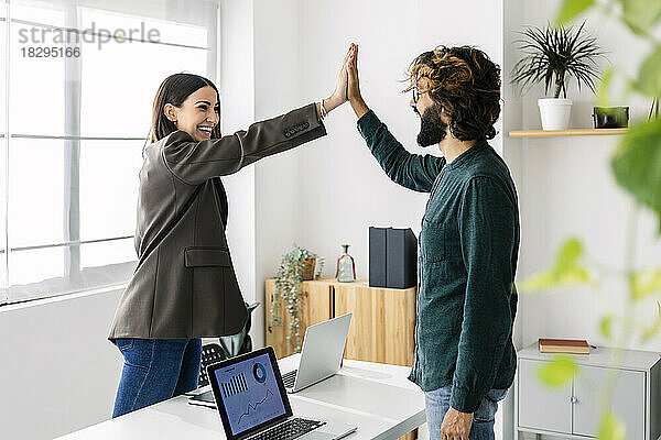 Happy businesswoman giving high-five to colleague in office