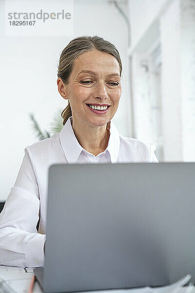 Glückliche Geschäftsfrau  die im Büro einen Laptop benutzt
