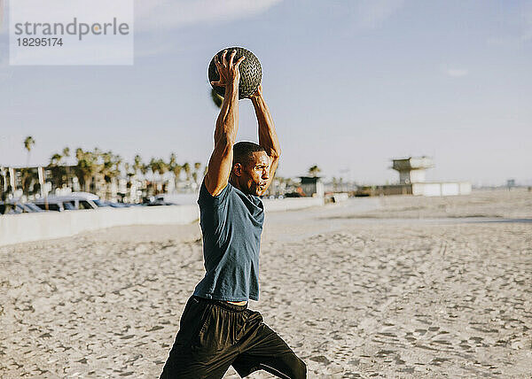 Sportler mit erhobenen Armen trainiert mit Ball am Strand
