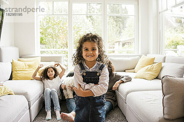 Glückliches Mädchen steht im Wohnzimmer mit der Familie im Hintergrund zu Hause