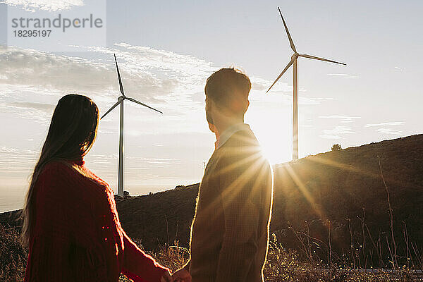 Couple holding hands looking at wind park at sunset