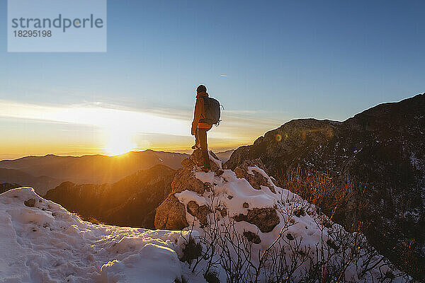 Wanderer steht bei Sonnenuntergang auf einem Felsen