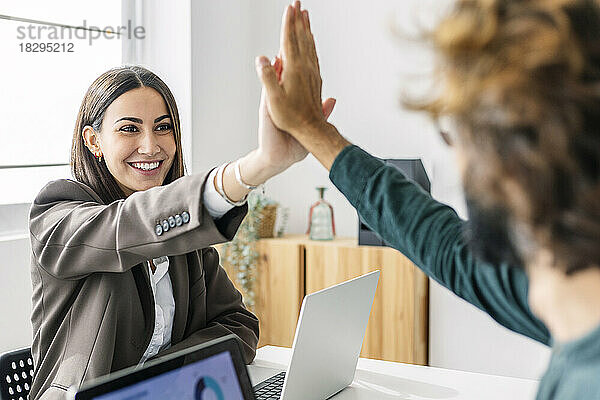 Lächelnde Geschäftsfrau gibt einem Kollegen am Arbeitsplatz High-Five