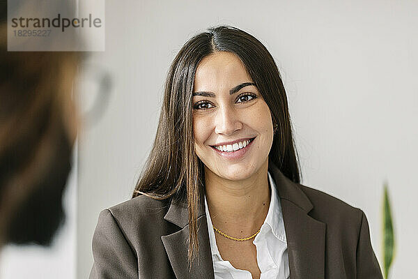 Lächelnde Geschäftsfrau blickt Kollegen vor weißer Wand an