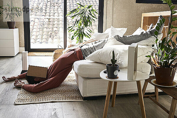 Mann bedeckt Gesicht mit Buch und liegt zu Hause auf dem Teppich