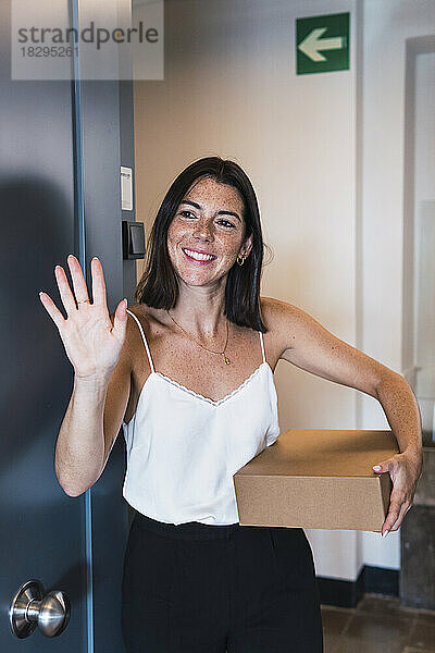 Glückliche Frau hält Paket in der Hand und winkt vor der Tür