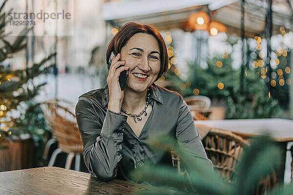 Glückliche reife Frau  die im Straßencafé mit dem Smartphone spricht