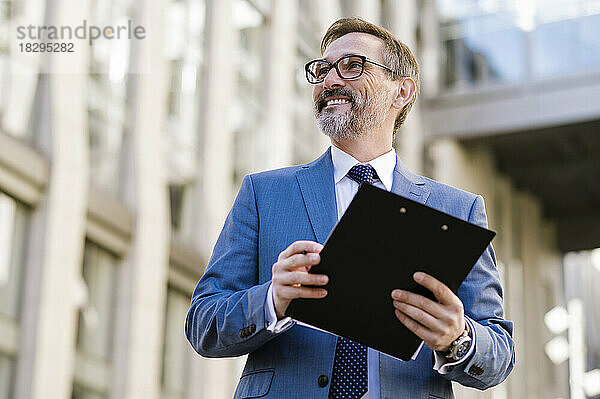 Happy businessman holding clipboard in front of building
