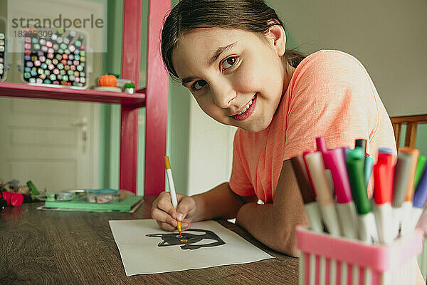 Lächelndes Mädchen  das zu Hause ein Katzenbild auf Papier ausmalt