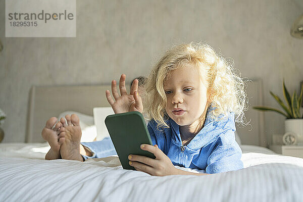Mädchen benutzt Smartphone und liegt zu Hause im Bett