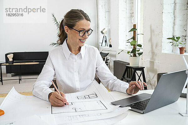 Glückliche Geschäftsfrau benutzt Laptop mit Blaupause im Büro