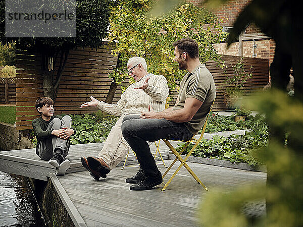 Vater  Sohn und Enkel sitzen am Gartenteich und unterhalten sich und entspannen sich