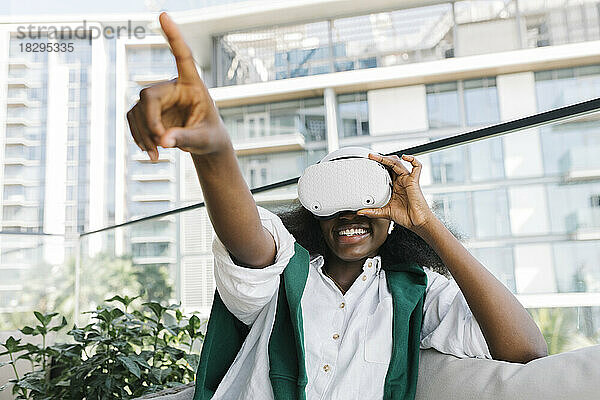 Glückliche Frau mit Virtual-Reality-Simulatoren gestikuliert auf dem Balkon