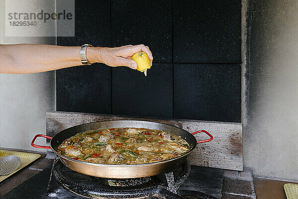 Frau drückt Zitrone auf Paella in Außenküche