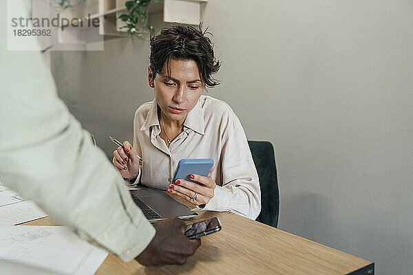 Businesswoman using smart phone with colleague at table