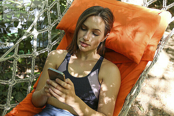 Woman wearing sports clothing using smart phone in hammock