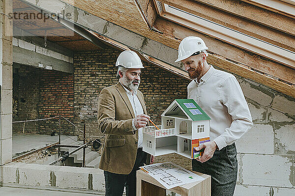 Glücklicher Architekt erklärt Hausmodell  das mit Kollegen auf der Baustelle steht