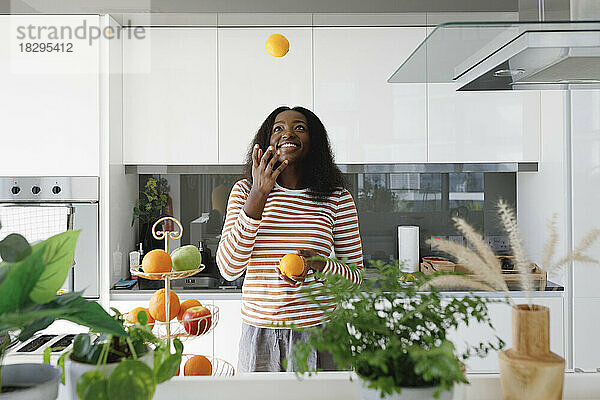 Glückliche Frau jongliert mit Orangen in der Küche