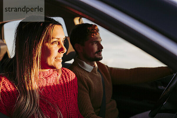 Couple driving in car with woman looking into sunlight